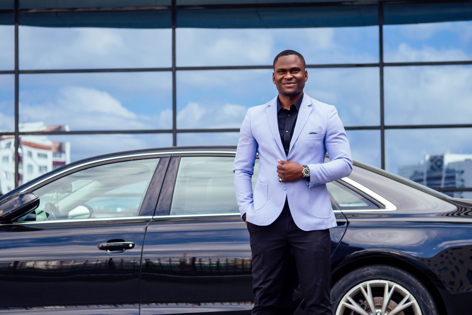 successful businessman handsome African American man in a stylish suit in a blue jacket standing in front of a cool new black car on the street